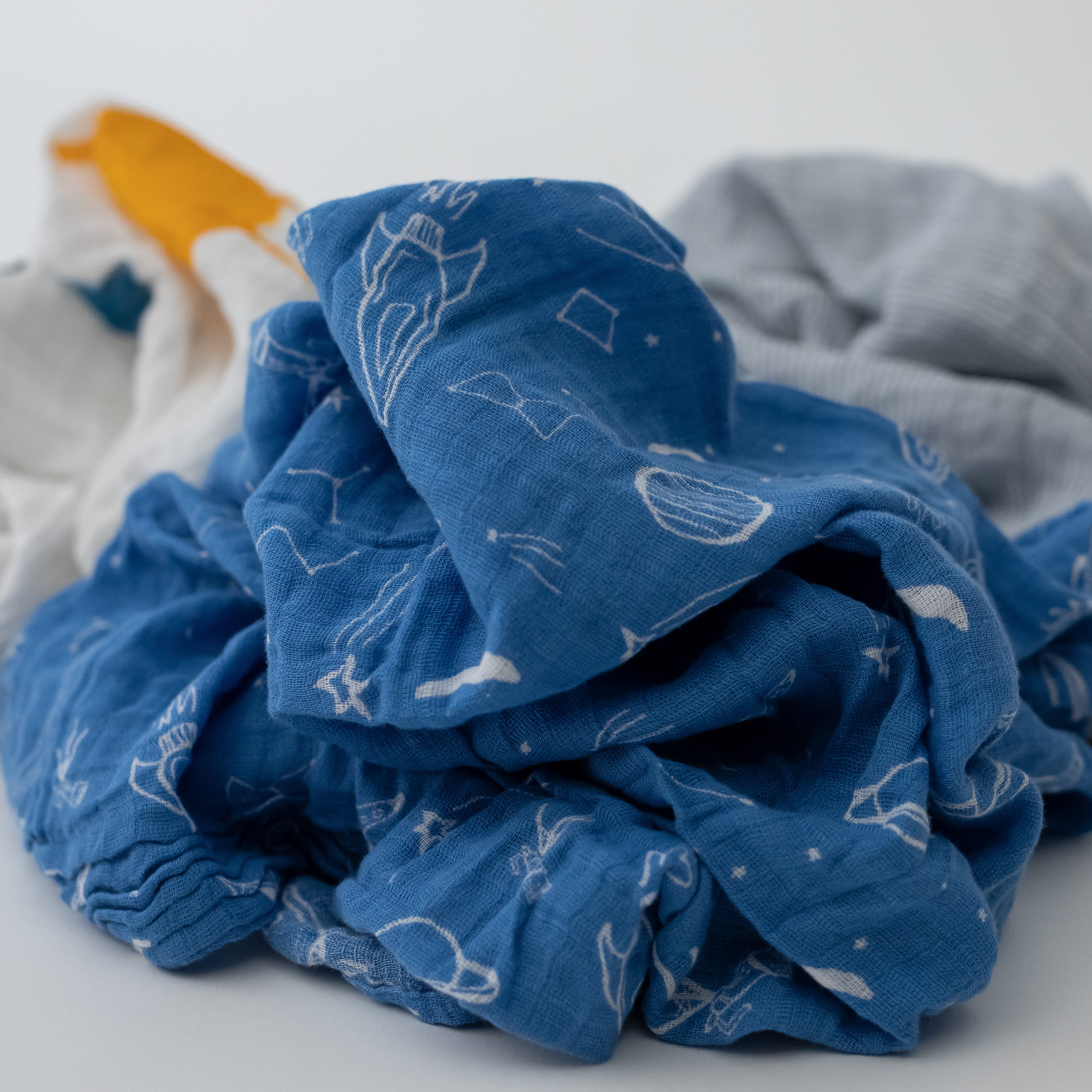 3 swaddle blankets focusing on the star gaze print with blue background and white stars, telescopes, planets, and rocket ships
