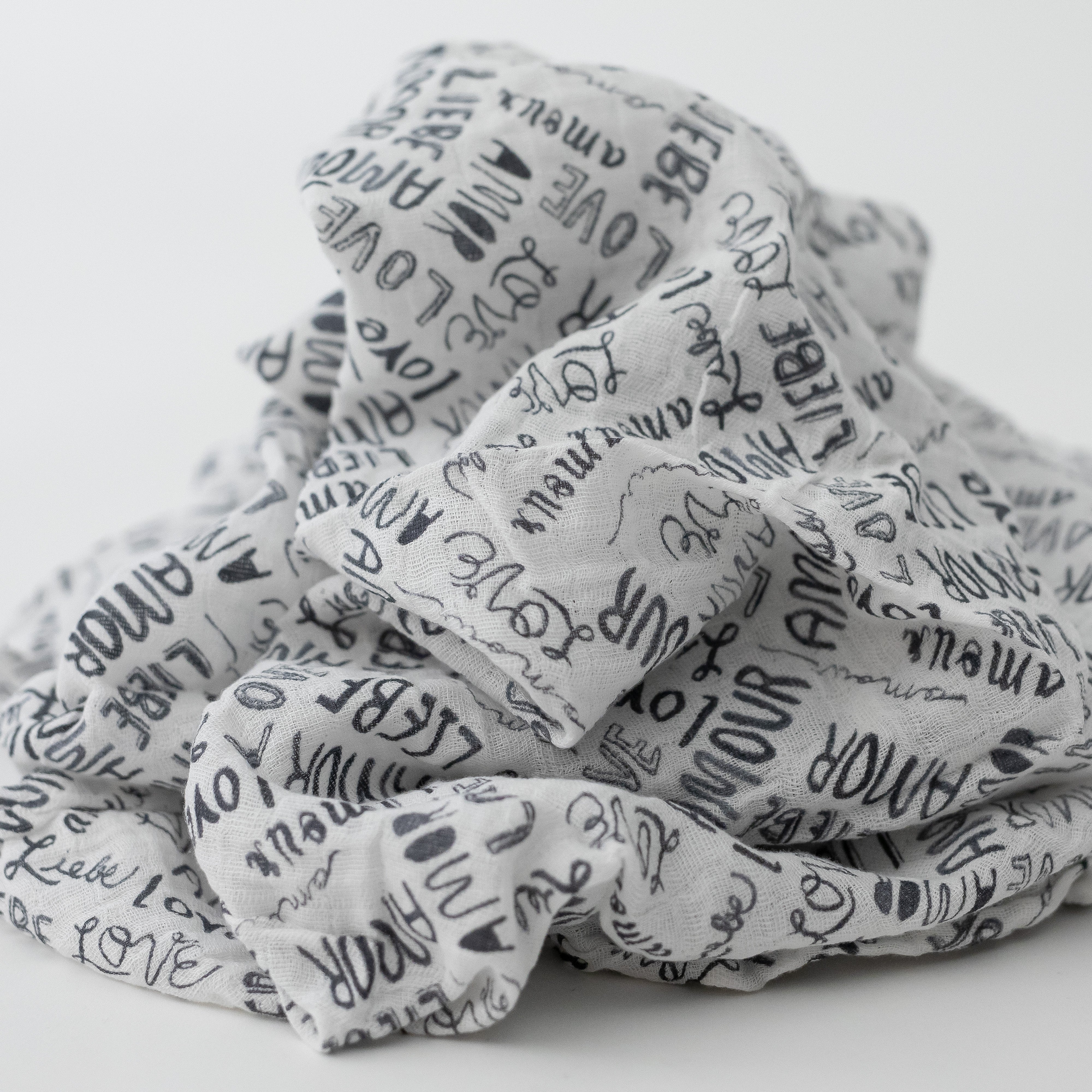 single swaddle blanket with the word "love" in multiple different languages in grey writing