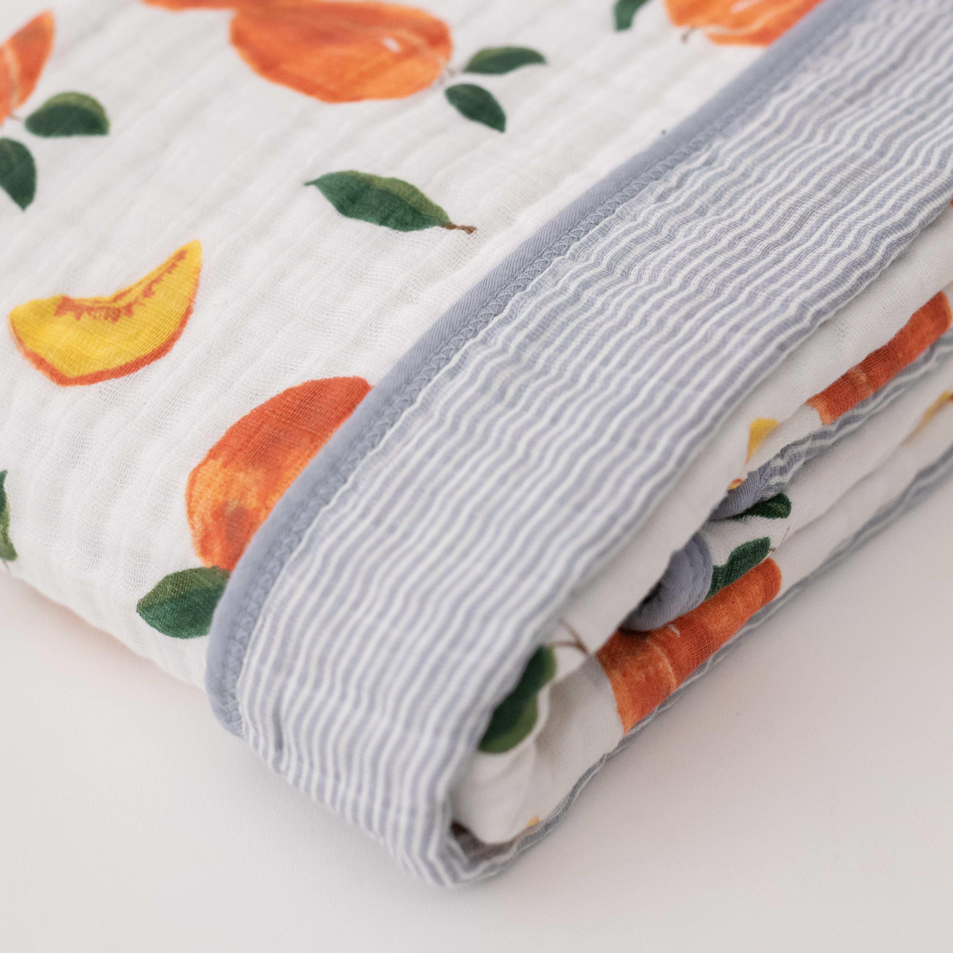 super soft cotton muslin quilt with whole and cut open peaches on one side and grey micro stripes on the other side