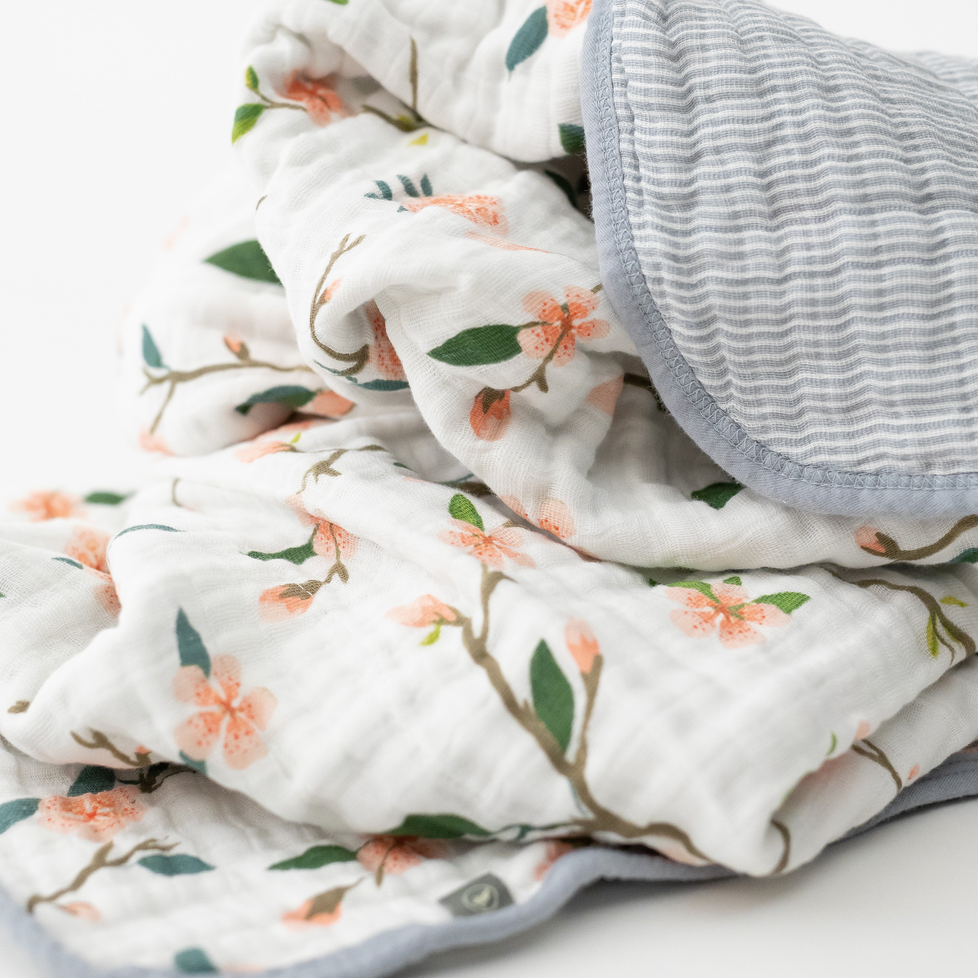 super soft cotton muslin quilt with peach blossoms blooming on a tree branch on one side and grey micro stripes on the other side