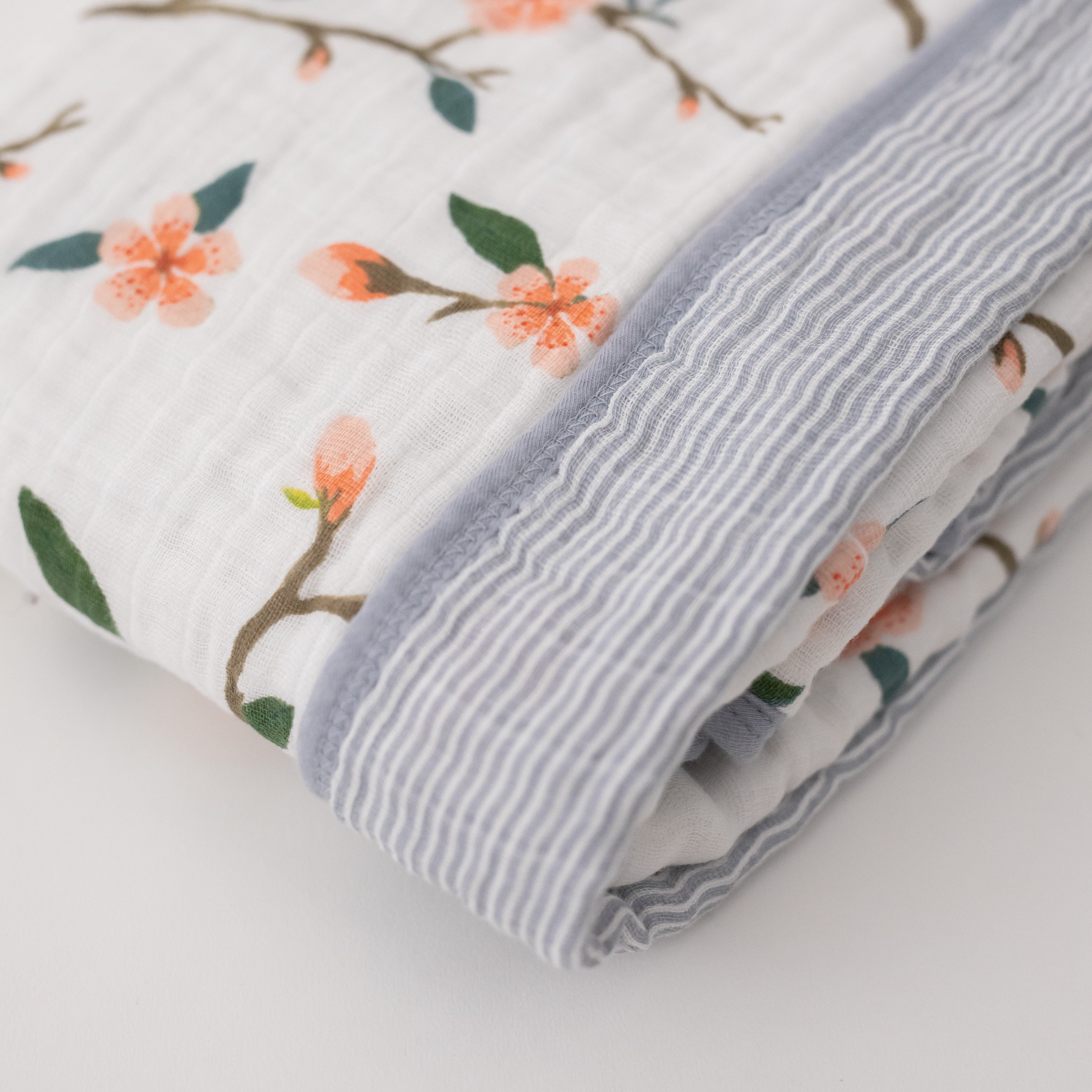 super soft cotton muslin quilt with peach blossoms blooming on a tree branch on one side and grey micro stripes on the other side