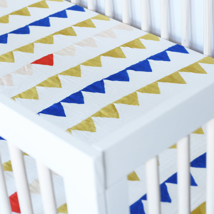 cotton muslin crib sheet with yellow and blue triangles strung together like a party banner in a crib