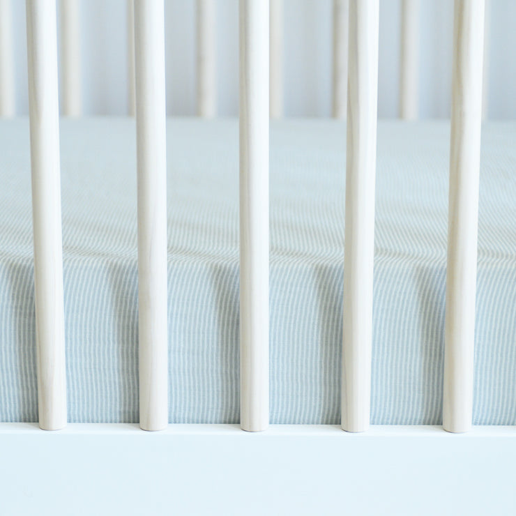 cotton muslin crib sheet with very small grey stripes in a crib