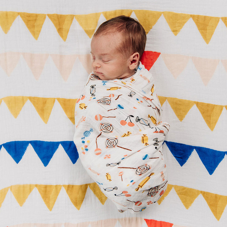 sleeping baby swaddled in a candy print blanket laying on a banners crib sheet