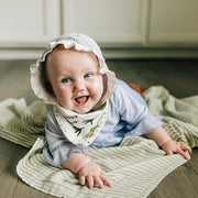 smiling baby wearing family farm reversible bandana bib with green stripe blanket