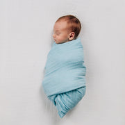sleeping baby swaddled in a blue mint blanket laying on a white crib sheet