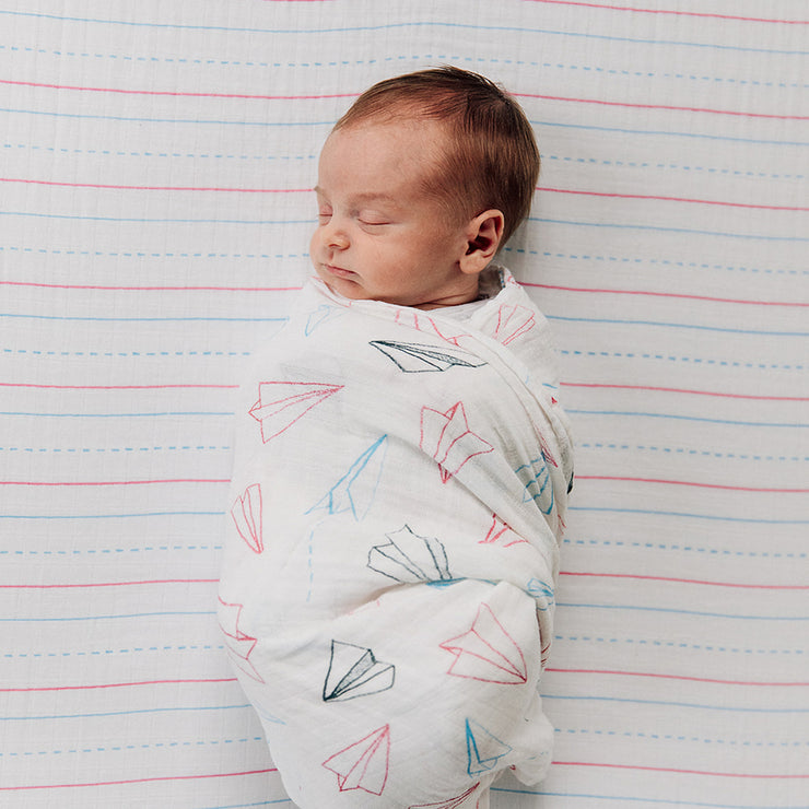 sleeping baby swaddled in a paper planes swaddle on a letter lines crib sheet