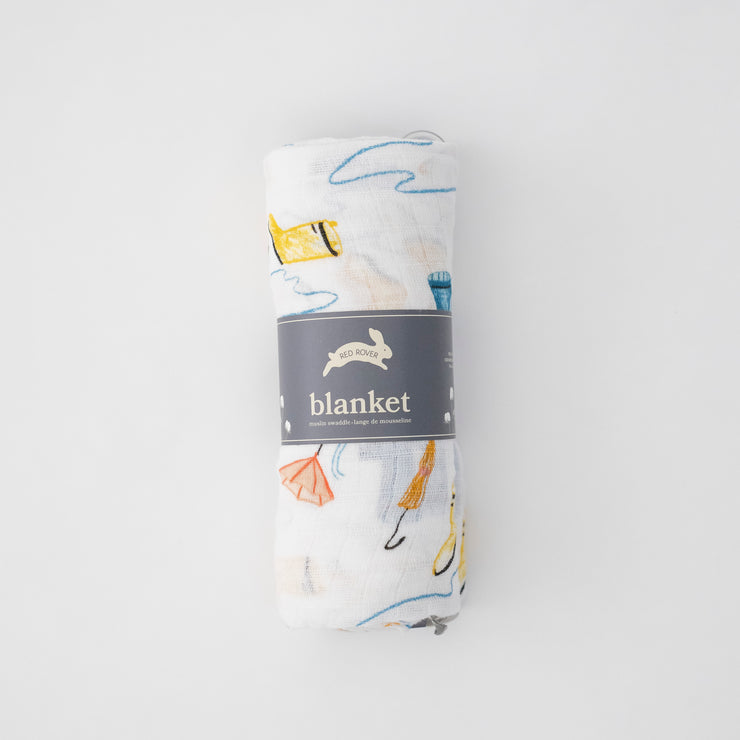 single swaddle blanket with yellow and blue rain boots, puddles, and orange umbrellas on a white background rolled in Red Rover packaging