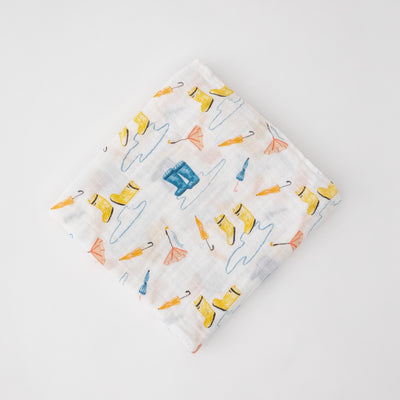 single swaddle blanket with yellow and blue rain boots, puddles, and orange umbrellas on a white background