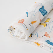 single swaddle blanket with yellow and blue rain boots, puddles, and orange umbrellas on a white background