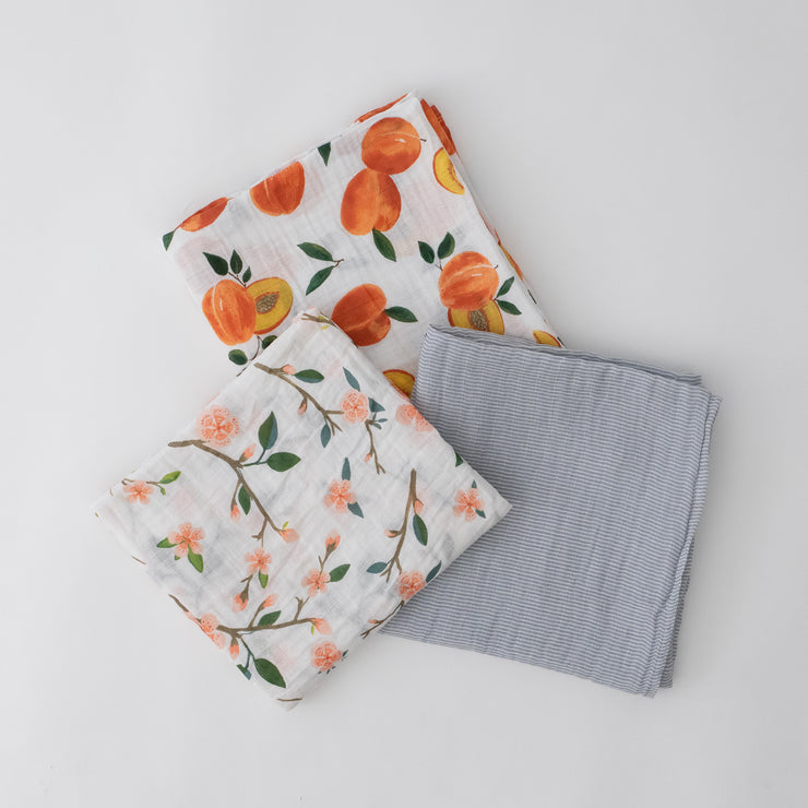 3 swaddle blankets featuring peach blossoms, whole and cut open peaches, and grey micro stripes