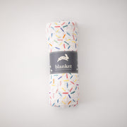 single swaddle blanket with lots of different colored sprinkles on a white background rolled in Red Rover packaging