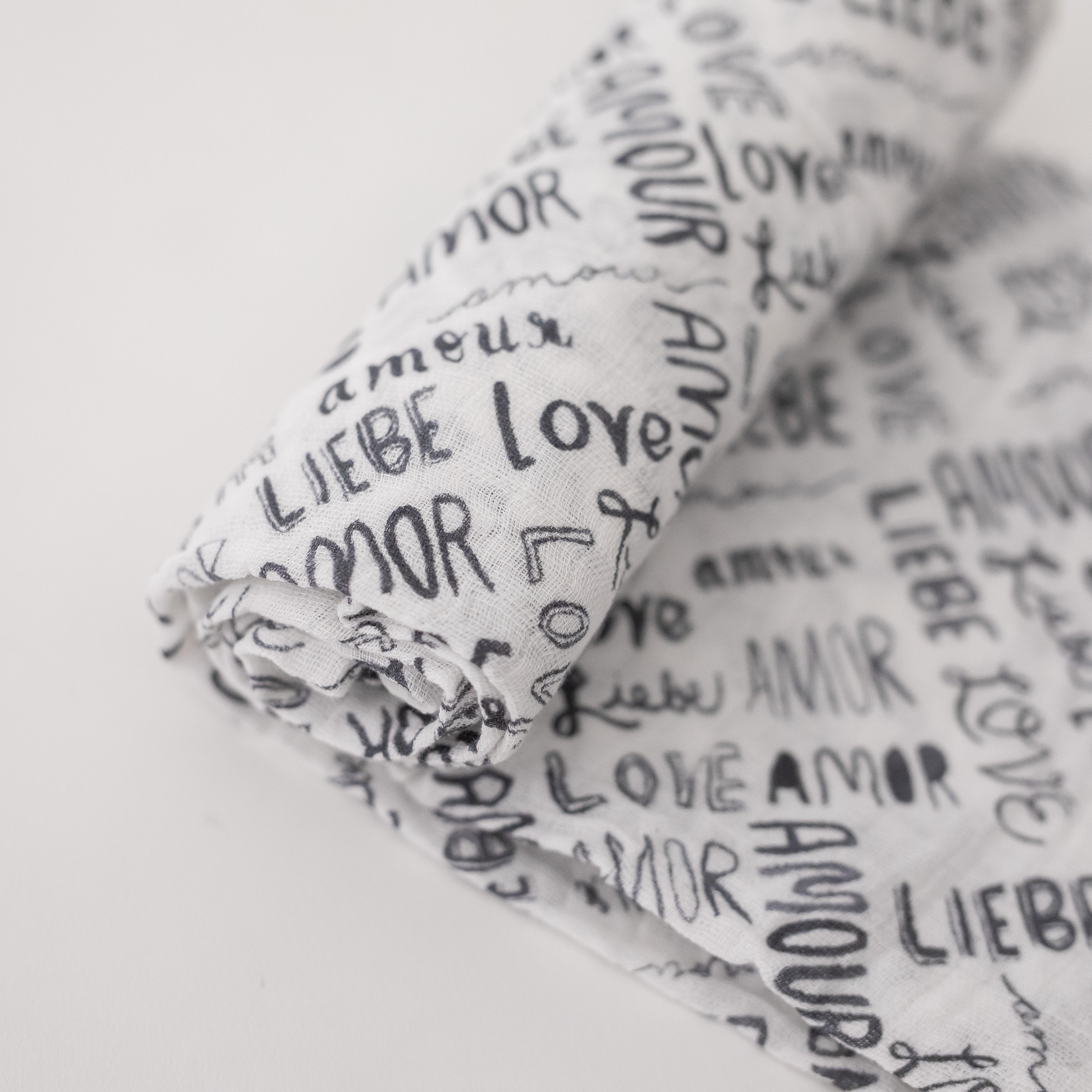 single swaddle blanket with the word "love" in multiple different languages in grey writing