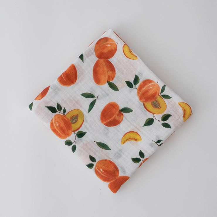single swaddle blanket with whole and sliced peaches on a white background