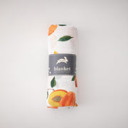 single swaddle blanket with whole and sliced peaches on a white background rolled in Red Rover packaging
