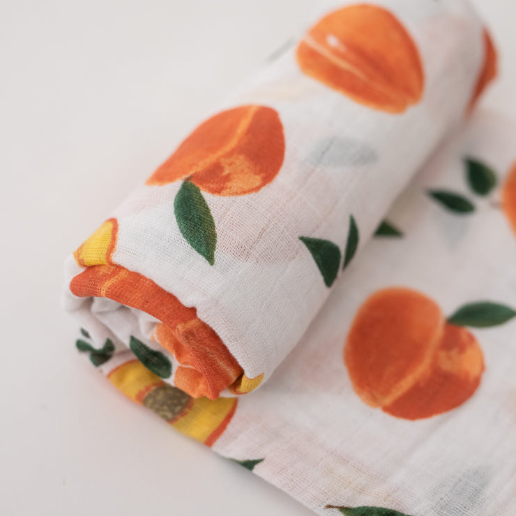 single swaddle blanket with whole and sliced peaches on a white background