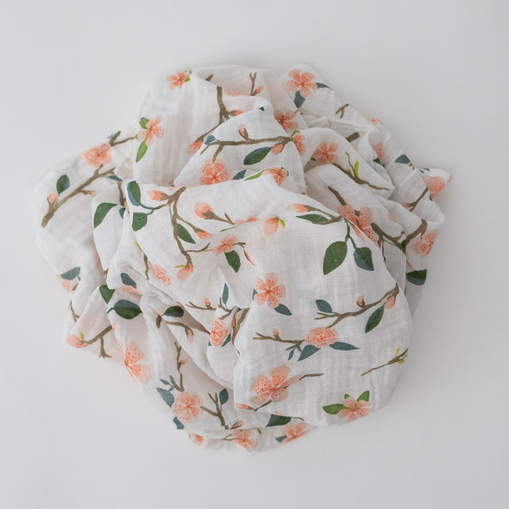 single swaddle blanket with peach blossoms blooming from a tree branch