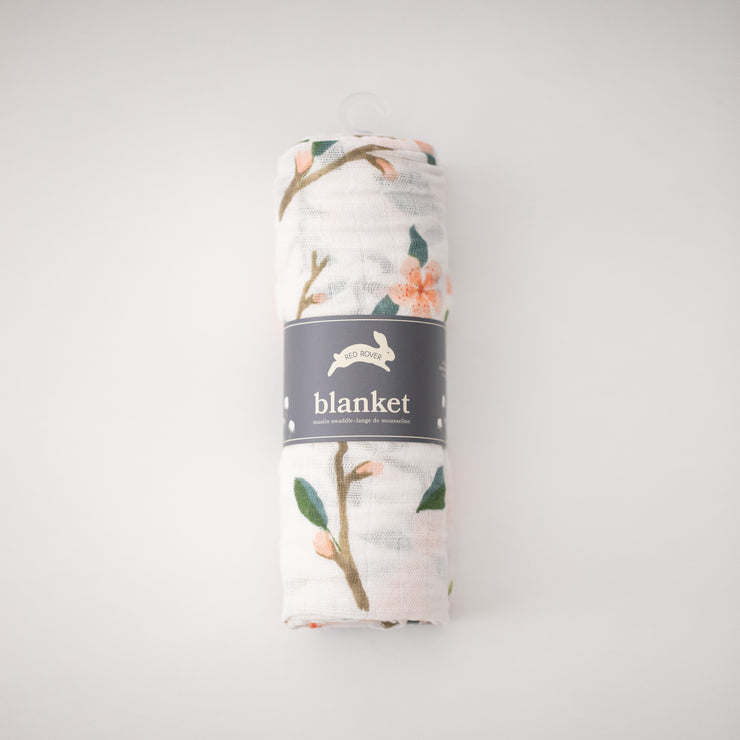 single swaddle blanket with peach blossoms blooming from a tree branch rolled in Red Rover packaging