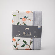 super soft cotton muslin quilt with peach blossoms blooming on a tree branch on one side and grey micro stripes on the other side in Red Rover packaging