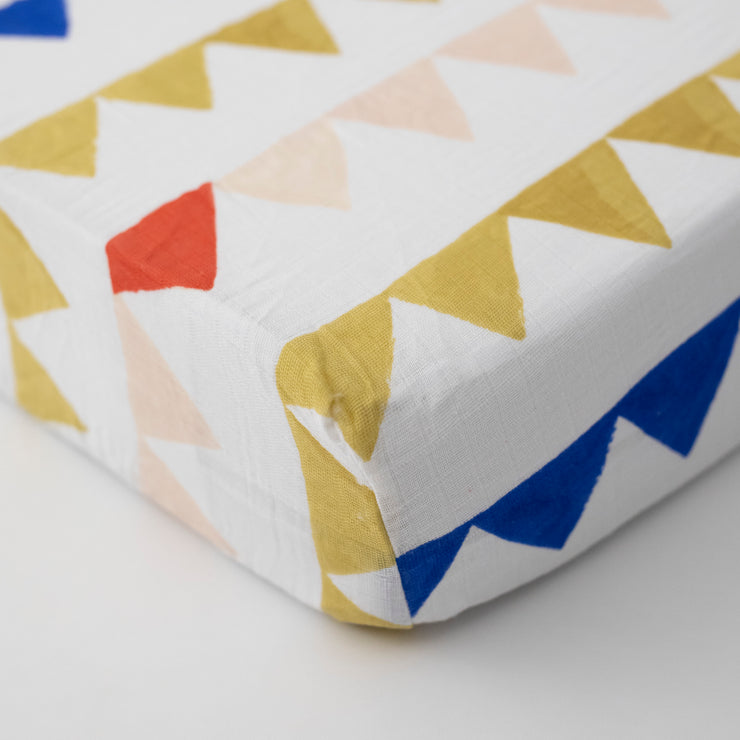 cotton muslin crib sheet with yellow and blue triangles strung together like a party banner