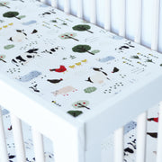 cotton muslin crib sheet with farm animals including cows, chickens, goats, sheep, and pigs in a crib