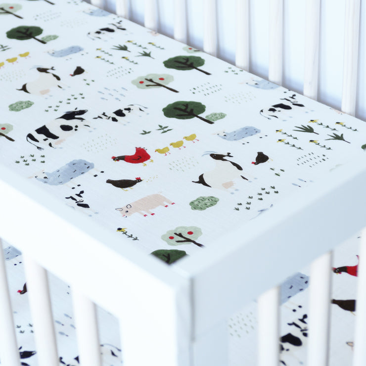 cotton muslin crib sheet with farm animals including cows, chickens, goats, sheep, and pigs in a crib