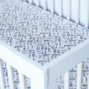 cotton muslin crib sheet with the word "love" in multiple different languages in grey writing on a white background in a crib