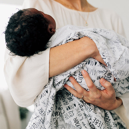 mom holding a baby with a love language swaddle blanket