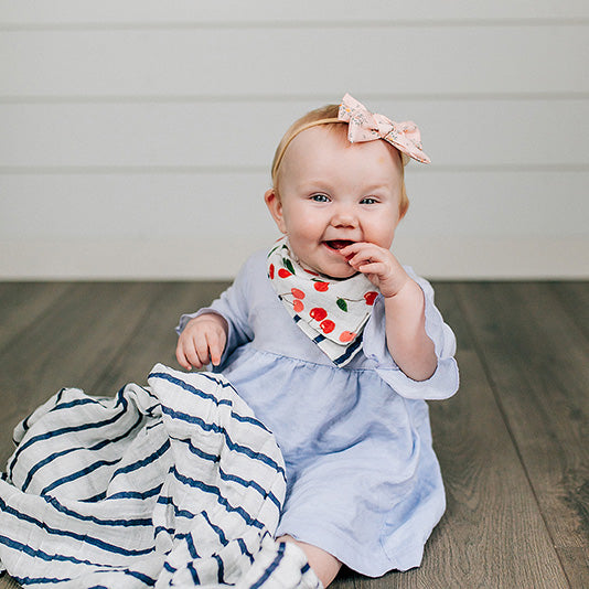 smiling baby wearing cherries reversible bandana bib with navy stripe blanket