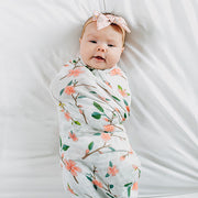 baby swaddled in a peach blossom laying on a white crib sheet