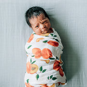 baby swaddled in a peaches blanket laying on a micro grey crib sheet