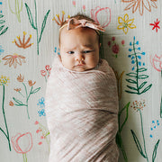 baby swaddled in a pink meadow blanket laying on a pastel petal crib sheet