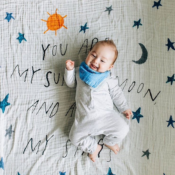smiling baby laying on a sun moon stars blanket wearing a star gaze bandana bib